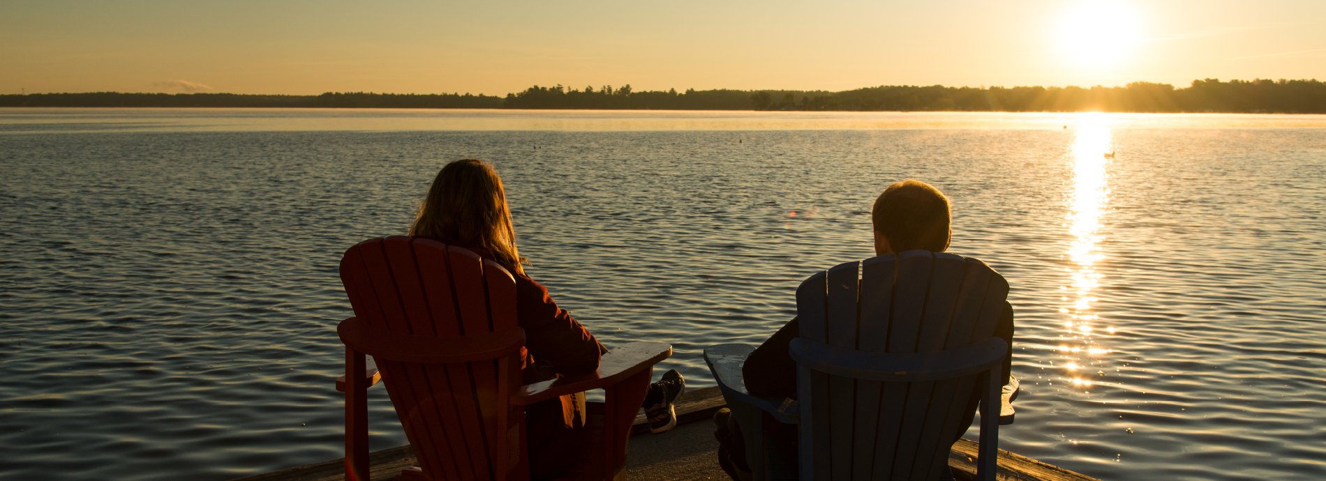 couple sitting in chairs on a dock at sunset